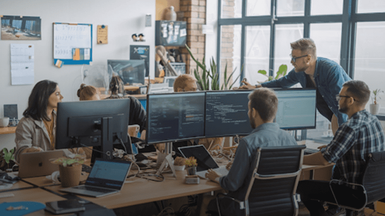 A-group-of-professionals-work-together-at-a-desk-with-computers,-emphasizing-teamwork-in-web-application-development