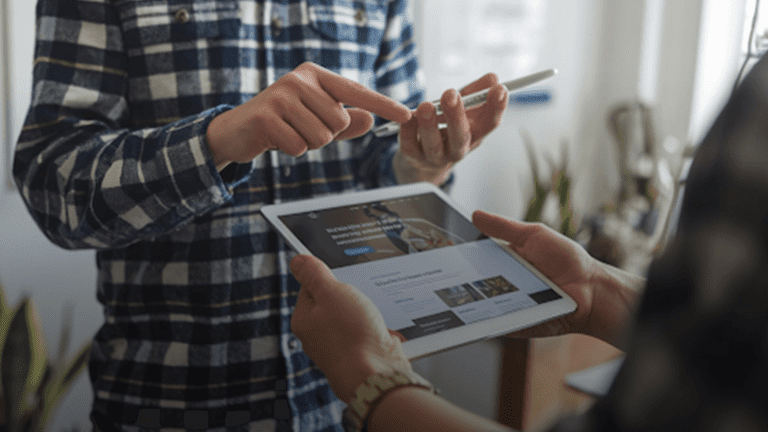 A-person-is-teaching-another-person-why-websites-need-to-be-user-friendly.-The-person-with-the-tablet-is-explaining-it-to-the-other-person-in-a-room-with-a-whiteboard-and-plants